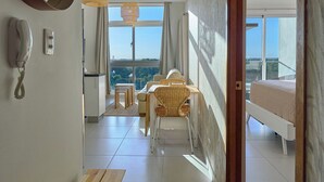 Una habitación de hotel moderna con un banco de madera, un comedor con sillas de mimbre, una cama y un ventanal con vistas a la ciudad.