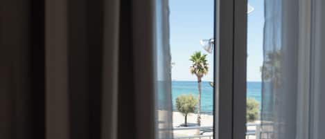 A view through a window with curtains, featuring a palm tree and a clear blue sky.