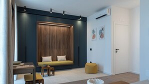 A modern living room with a dark blue accent wall, a wooden panel wall, a yellow sofa, a small wooden table, and a yellow pouf. - Leluan Bed & Breakfast (Mola di Bari)