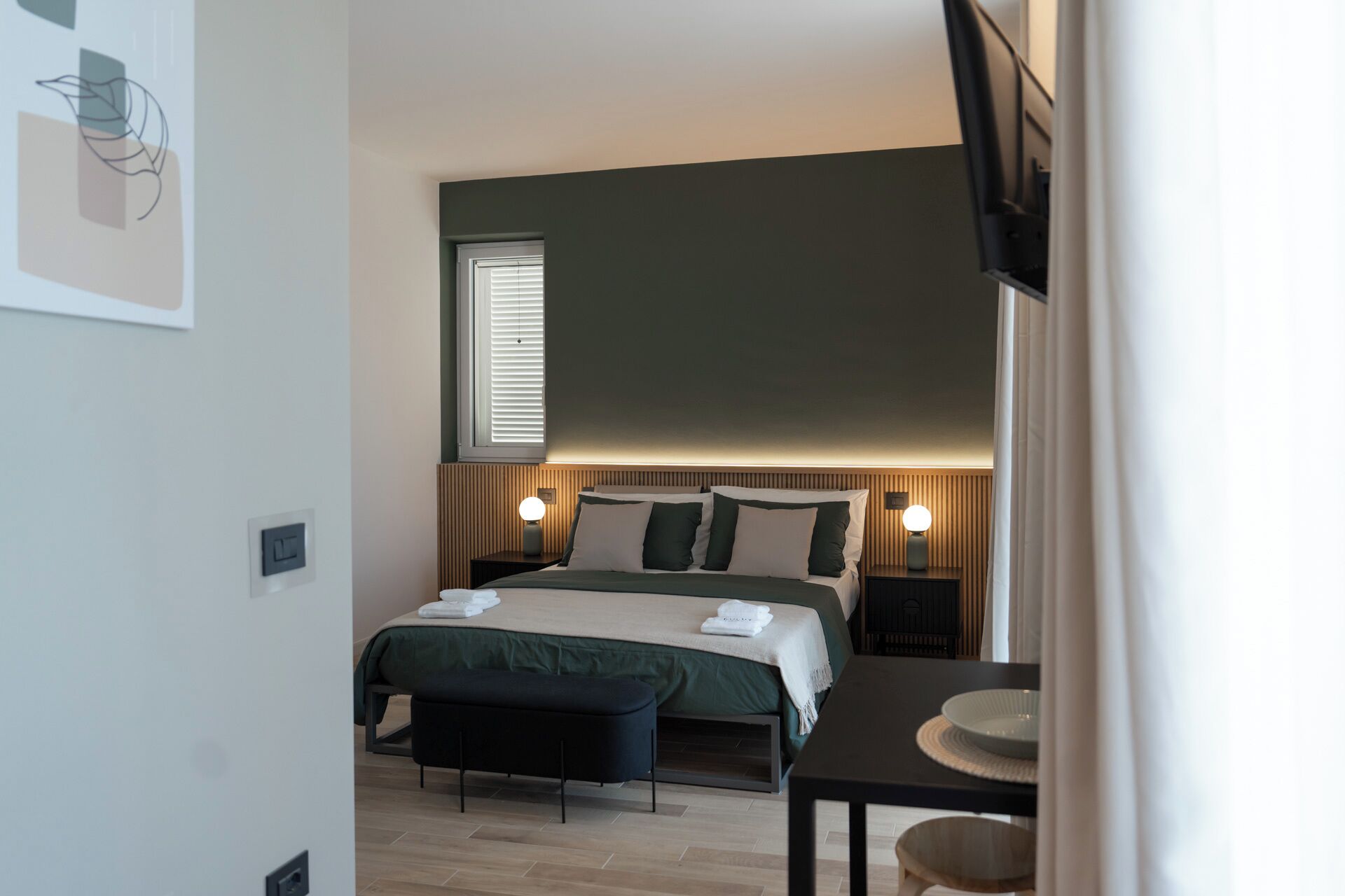 A modern bedroom with a bed, bedside tables, a bench, and a desk.