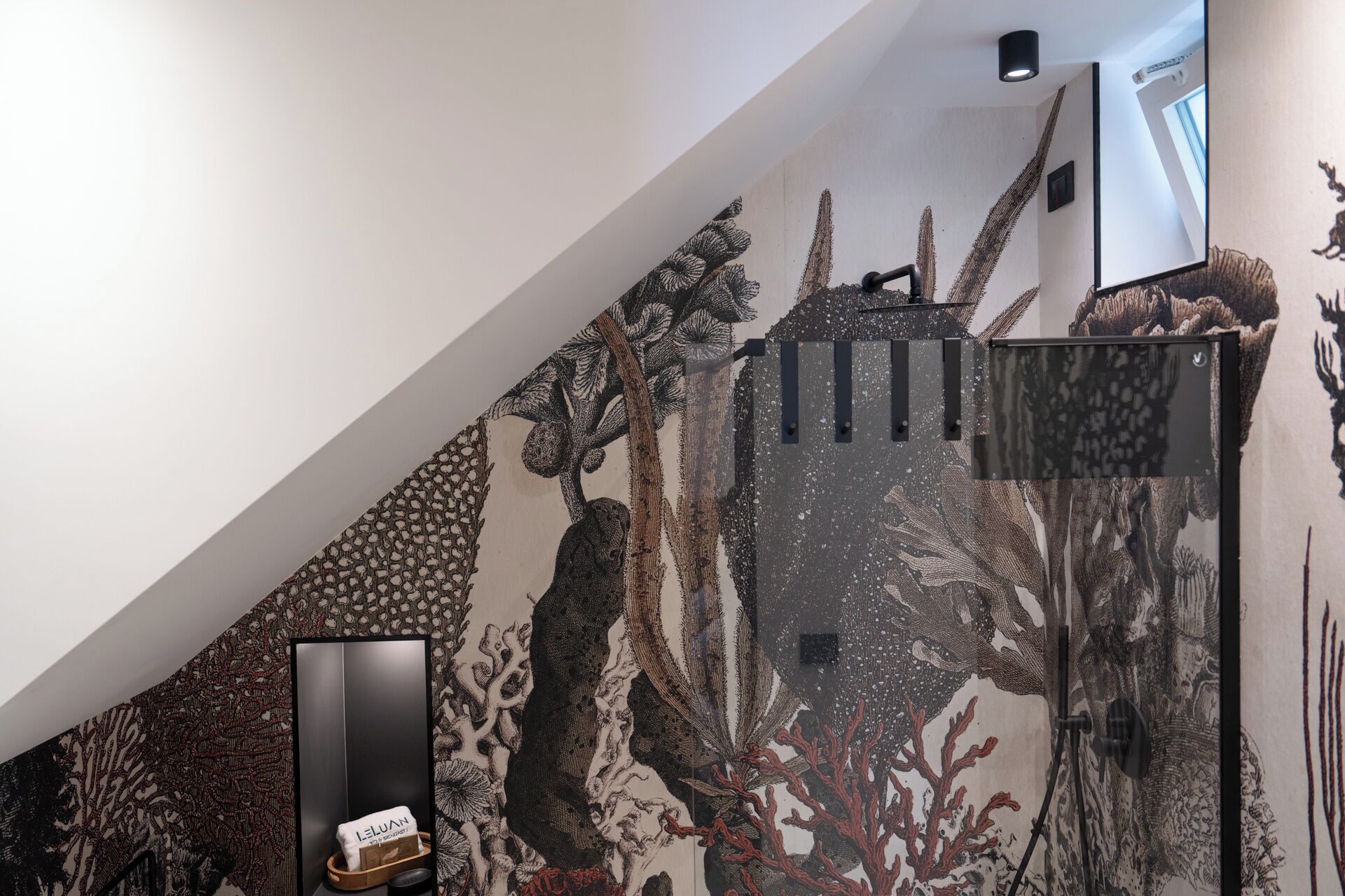 A room with a large, detailed mural on the wall, a black-framed picture, and a small wooden box with a cushion.