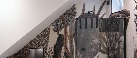 A room with a large, detailed mural on the wall, a black-framed picture, and a small wooden box with a cushion.