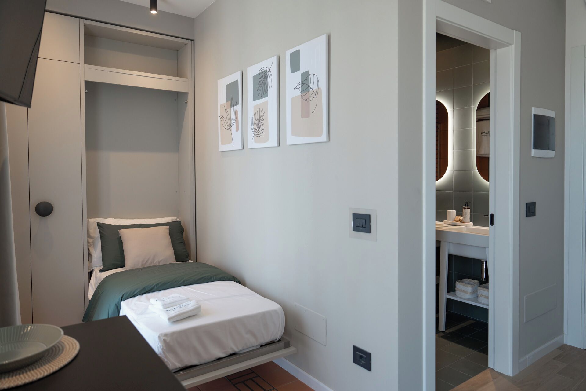 Un dormitorio moderno con cama, escritorio y vestidor. Hay tres obras de arte enmarcadas en la pared.