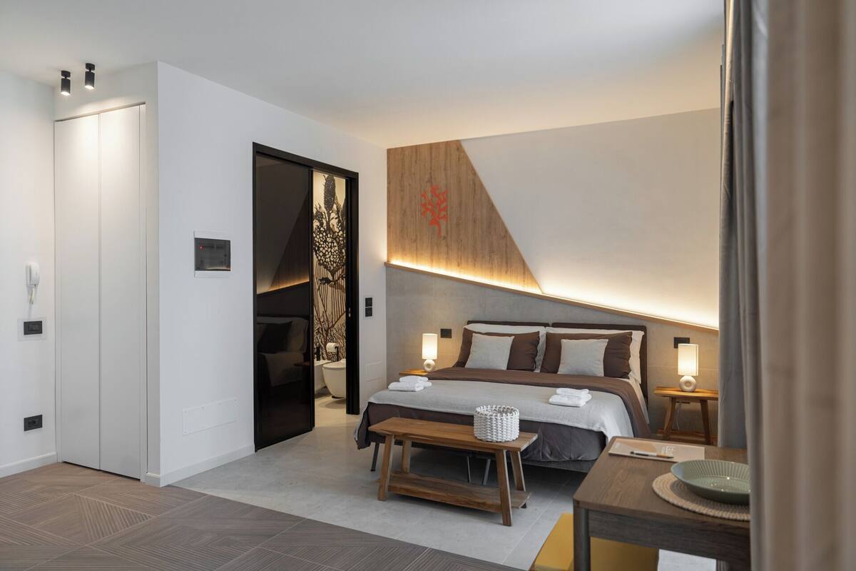 A modern hotel room with a bed, bedside tables, a bench, and a wooden accent wall.