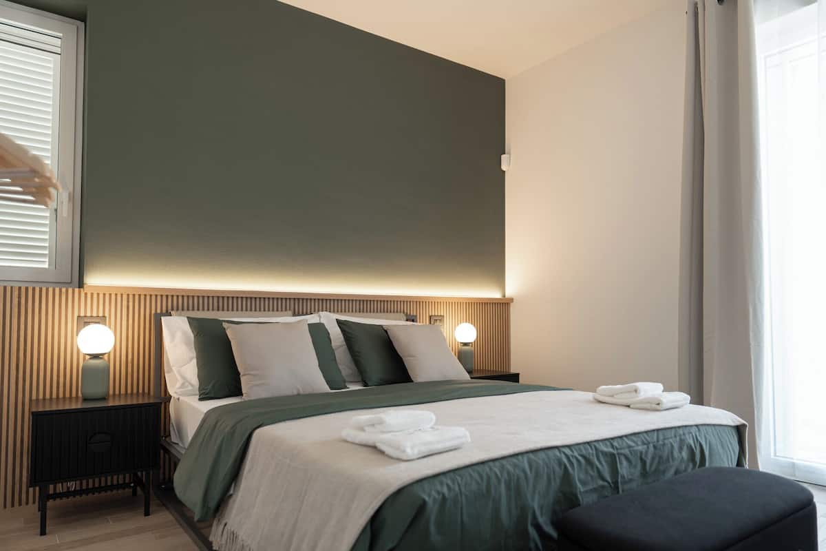 A modern bedroom with a bed, bedside lamps, and a window with curtains.