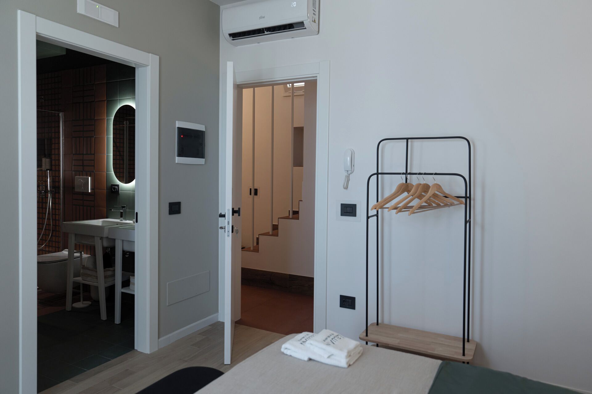 A hotel room with a bathroom, a coat rack, and a bed.