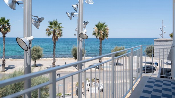 A balcony with a view of the sea, palm trees, and a parking area. - Leluan Bed & Breakfast (Mola di Bari)