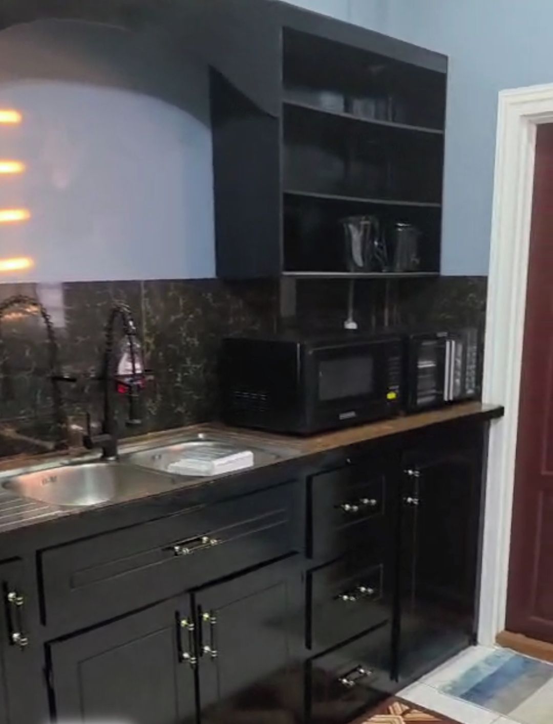 Une cuisine moderne avec des meubles de rangement aux couleurs sombres, un four à micro-ondes encastré et un évier.
