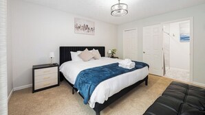 Quarto com cama, mesa de cabeceira, cômoda e luminária no teto.