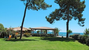 Un espacio con césped, vista al mar, un pabellón y un parque infantil.