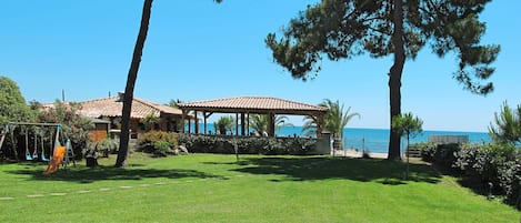 A grassy area with a beach view, a pavilion, and a playground.