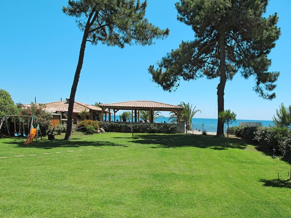 A grassy area with a beach view, a pavilion, and a playground.