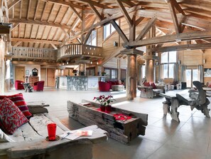 A spacious interior with wooden beams, a stone fireplace, and red furniture.