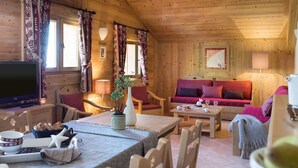 L’intérieur d’un chalet en bois chaleureux et accueillant, avec un coin repas, un canapé et un téléviseur.