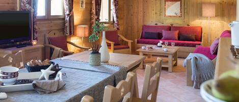 A cozy wooden cabin interior with a dining area, sofa, and television.