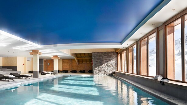 Une piscine intérieure avec des chaises longues et un mur en pierre.