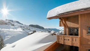 Un chalet en bois doté d’un balcon donnant sur un paysage montagneux enneigé.