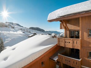 Een houten chalet met een balkon met uitzicht op een besneeuwd berglandschap.
