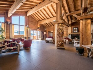 A spacious wooden interior with a high ceiling, large windows, and a fireplace.