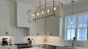 Una cocina moderna con una isla grande, taburetes de madera, armarios blancos e iluminación colgante.