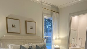 Una cama bien hecha con ropa de cama blanca y gris, un cabecero de madera y una mesita de noche con una lámpara.