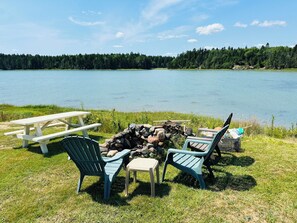 A lakeside picnic area with a fire pit, picnic table, and chairs. - Charming 3-bedroom cottage in Roque Bluffs with ocean access and fire pit (Roque Bluffs)