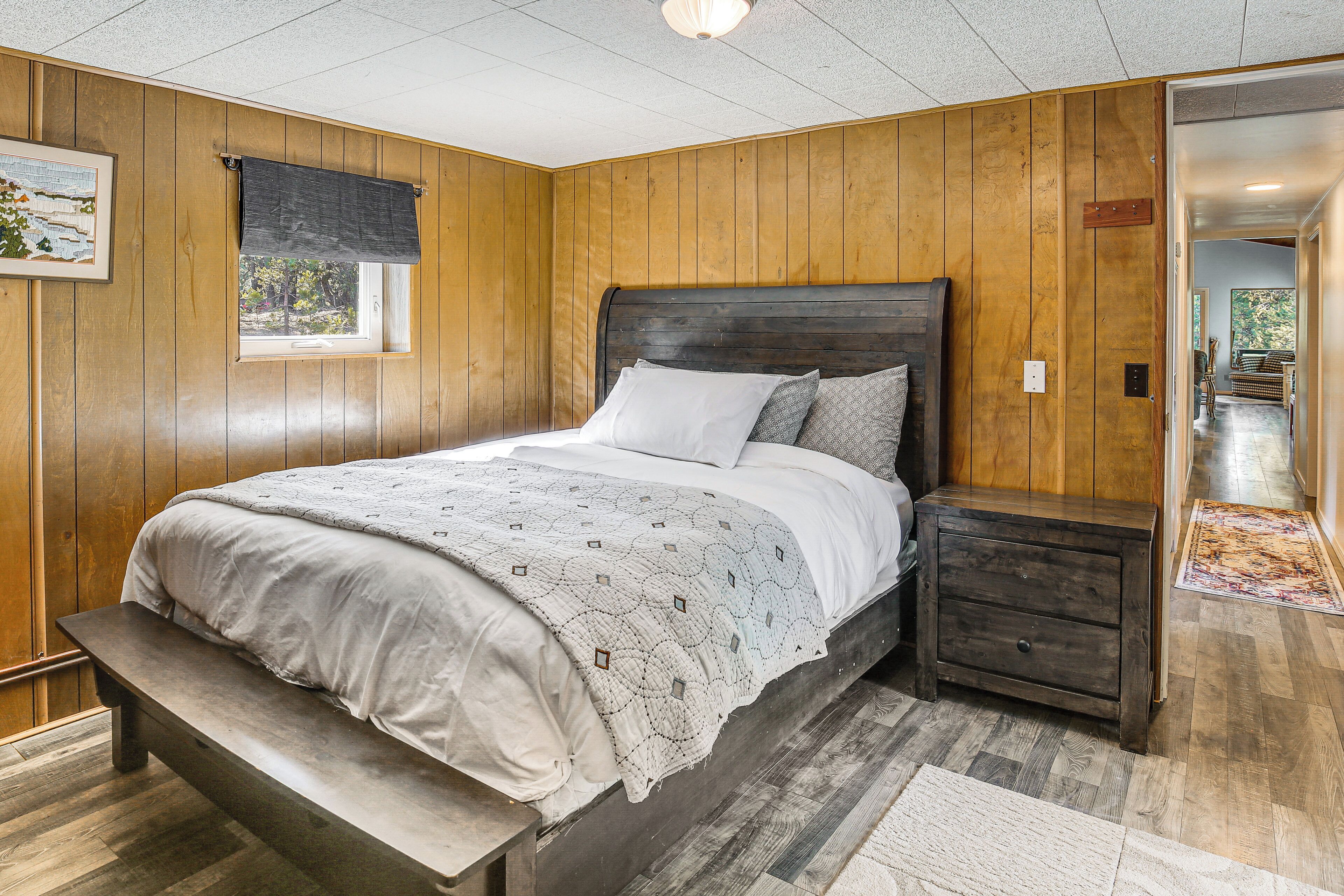 Un dormitorio con paneles de madera, una cama, una mesita de noche, un banco y vistas al exterior a través de una ventana.