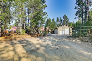 A gravel driveway leading to a wooden barn with a metal gate, surrounded by tall pine trees. - Woodsy Cabin Retreat ~ 4 Mi to Crescent Lake! (Crescent)