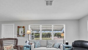 A living room with a grey sofa, two side tables, a wicker chair, and a black leather chair. - Kayaks & Access to Beach on Matlacha Pass (Saint James City)