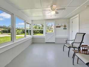 A room with large windows, a ceiling fan, and a door leading outside.