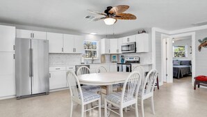 A modern kitchen with white cabinetry, a stainless steel refrigerator, a microwave, and a dining table with four chairs. - Kayaks & Access to Beach on Matlacha Pass (Saint James City)