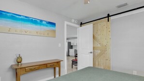 A bedroom with a bed, a wooden desk, a wall-mounted picture, and a sliding door leading to a kitchen. - Kayaks & Access to Beach on Matlacha Pass (Saint James City)