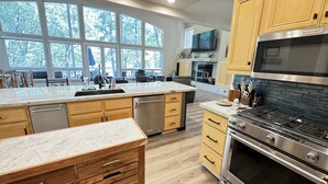 A modern kitchen with a large island, stainless steel appliances, and a view of the outdoors through large windows. - Large Lakefront Paradise, 4000+ Sq Feet, Kayaks (Lakehead)