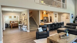 A spacious living area with a high ceiling, a staircase leading to an upper level, a kitchen area, and a seating area with a coffee table. - Large Lakefront Paradise, 4000+ Sq Feet, Kayaks (Lakehead)
