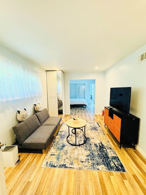 Cozy living space with a sofa, round table, and TV cabinet, leading to a separate bedroom.