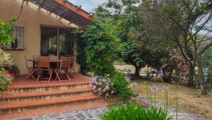Une terrasse avec une table et des chaises, entourée d’un jardin où poussent différentes plantes et fleurs.