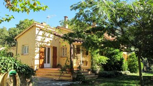Une maison jaune avec un toit rouge, une cheminée et une véranda.