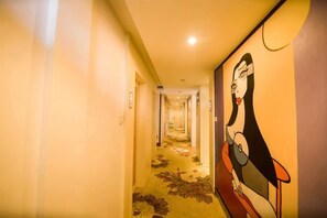 Um corredor longo em um hotel, com carpete floral e um mural na parede.