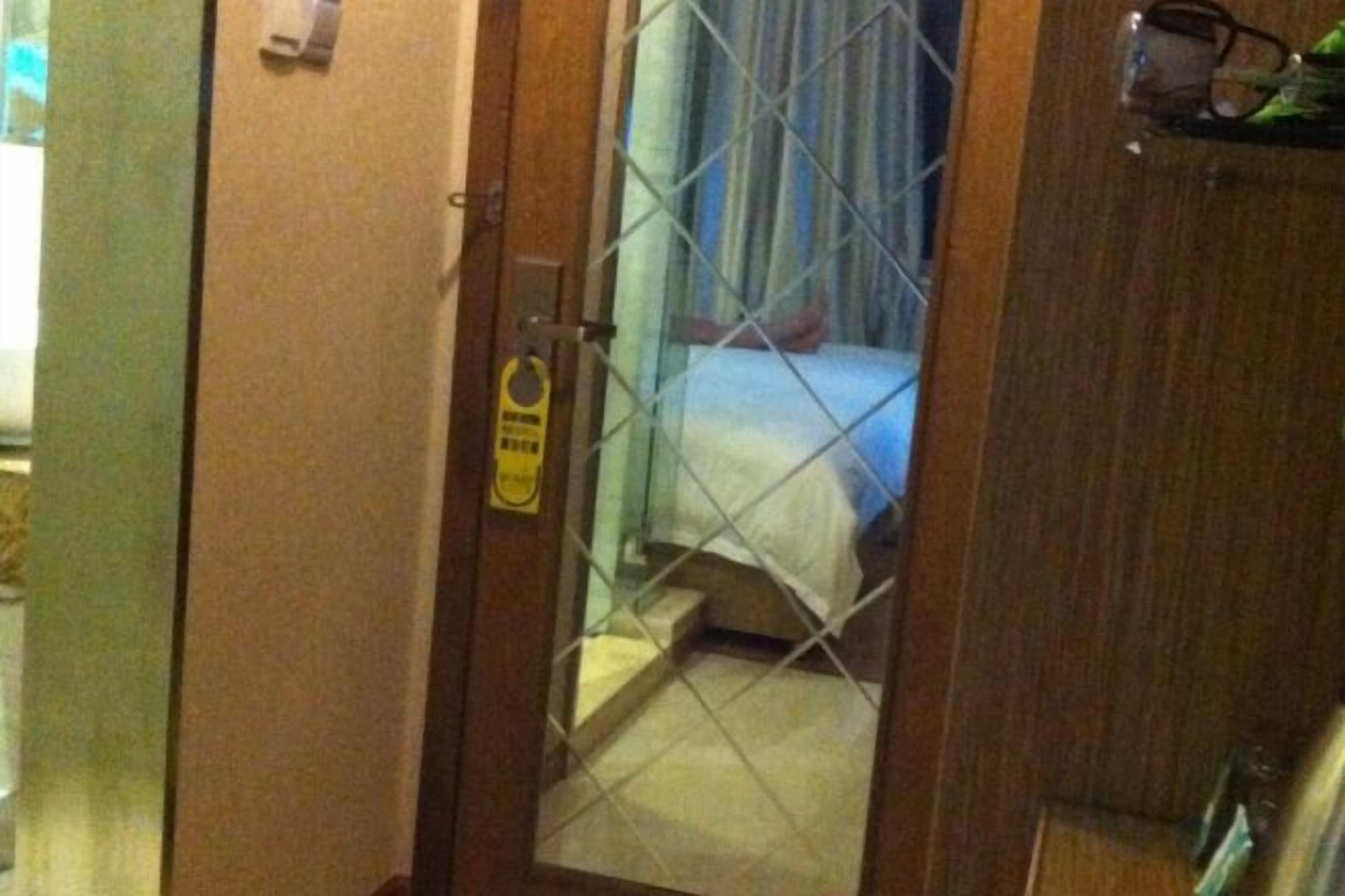 A hotel room with a bed, a door with a lock, and a small window with curtains.
