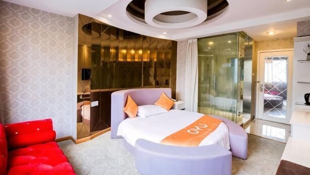Habitación de hotel moderna con una cama grande, zona de estar, separador de vidrio y vistas al exterior.