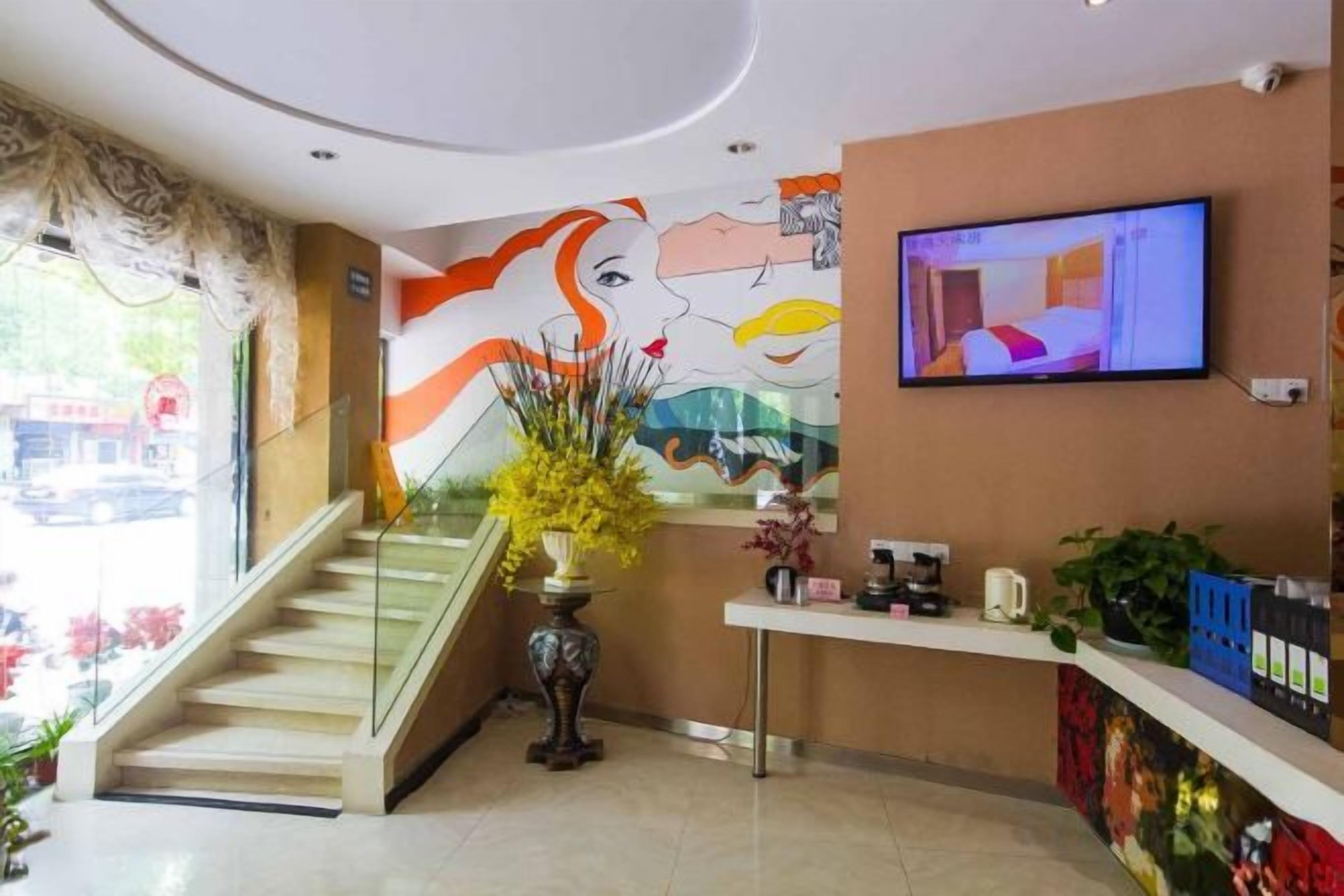 Eine Hotelhalle mit Treppe, einer Rezeption, einem Fernseher und einem Wandgemälde.
