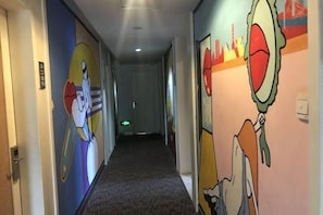 Un pasillo de hotel con murales coloridos en las paredes, pisos alfombrados y puertas a la izquierda.