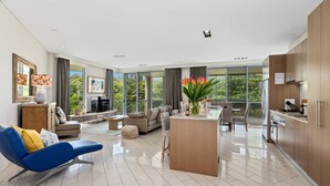 Ein modernes Wohnzimmer mit einer Couch, einem blauen Sessel, einem Essbereich und einer Küche mit Holzschränken.