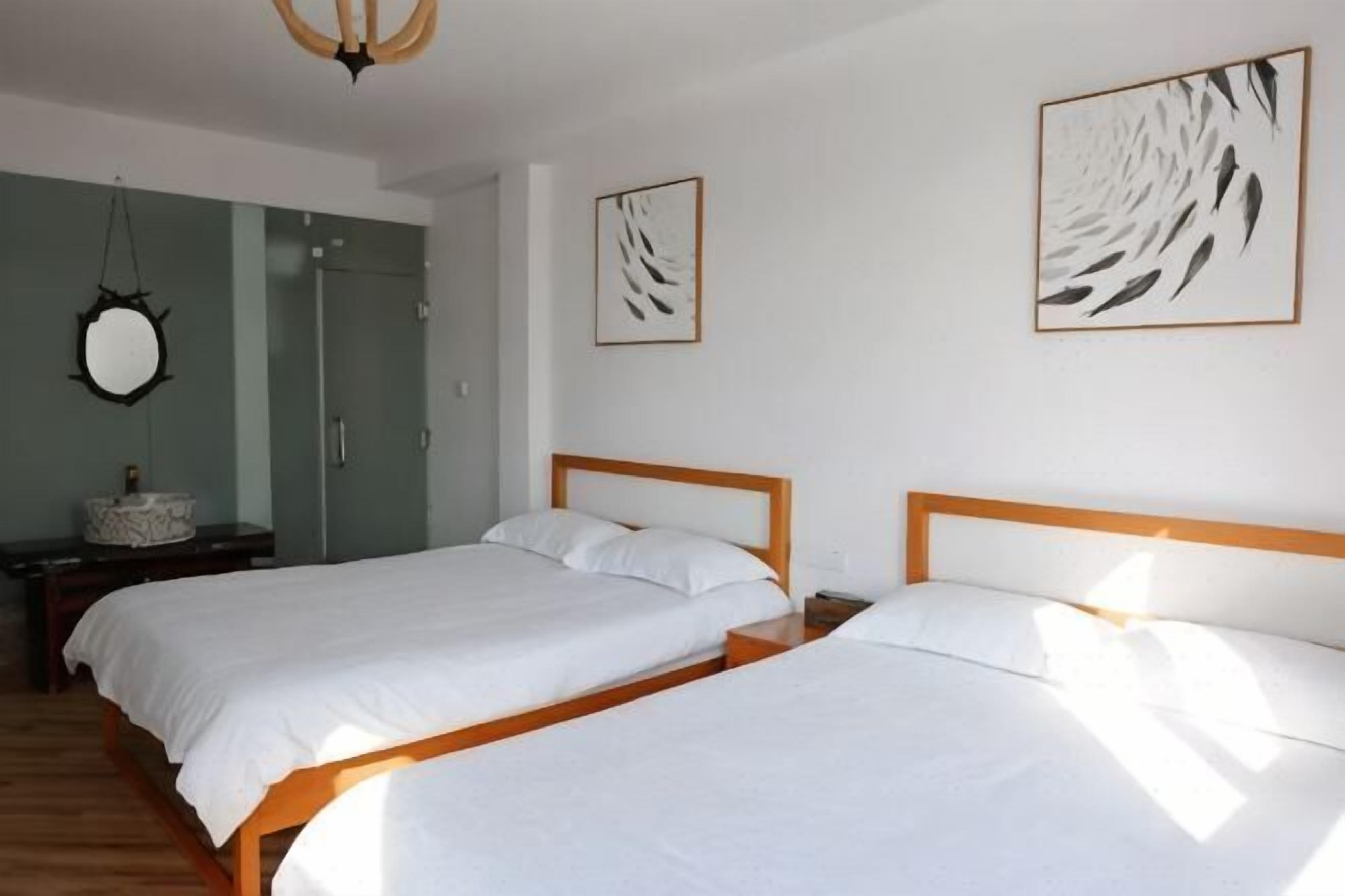 A bedroom with two beds, a mirror, and artwork on the walls.