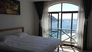 A bedroom with a large bed, a window with a view of the sea, and a balcony. - Shensi Gouqi Island Mr.Tang's Private Garden Inn (Shengsi)