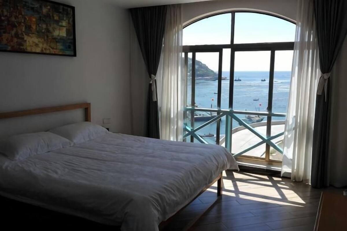 Ein Schlafzimmer mit einem großen Bett, einem Fenster mit Meerblick und einem Balkon.