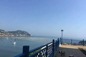 A coastal view from a wooden deck with a blue railing, overlooking calm waters and distant hills. - Shensi Gouqi Island Mr.Tang's Private Garden Inn (Shengsi)