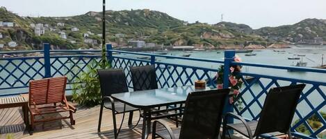 Una terraza con mobiliario exterior, con vistas a una masa de agua con barcos y colinas al fondo.