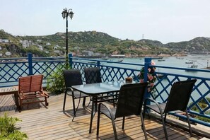 A deck with a table and chairs overlooking a body of water with boats and hills in the background. - Shensi Gouqi Island Mr.Tang's Private Garden Inn (Shengsi)