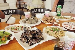 Una mesa de comedor con diversos platos, incluyendo mariscos y ensaladas, y dos sillas con la etiqueta 'USINE'.